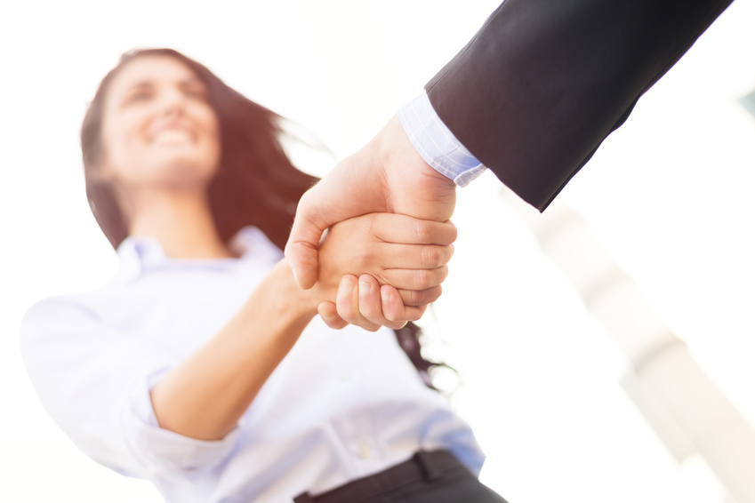 Business woman with face out of focus shakes hands with business man who can see only the hand.